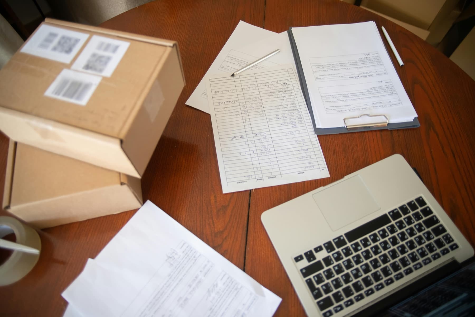 Small business paperwork arranged beside shipping boxes and a laptop.